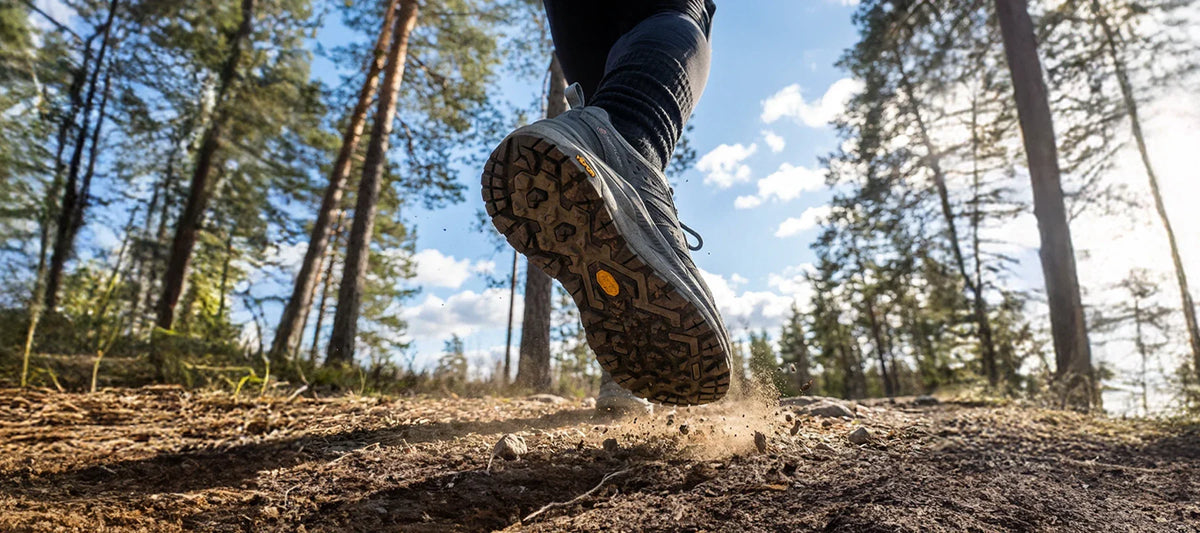 Hiking boot sole with Vibram logo walking away on woodland trail with trees and blue sky