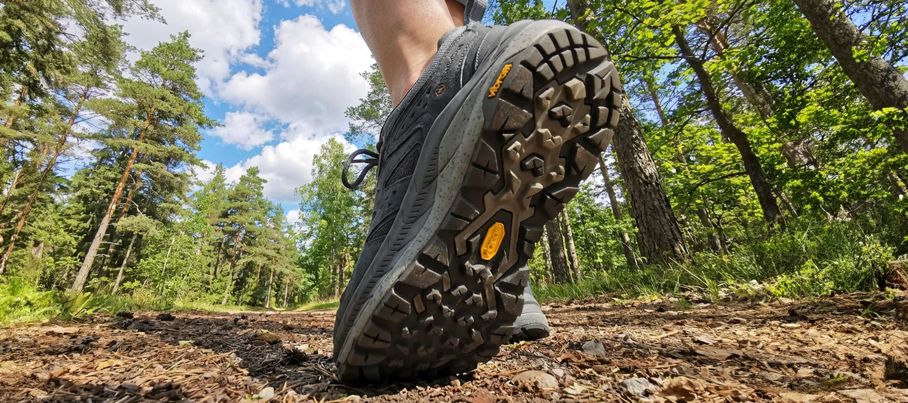 Sole view of Vibram walking boots on a woodland trail with trees and blue sky in the background