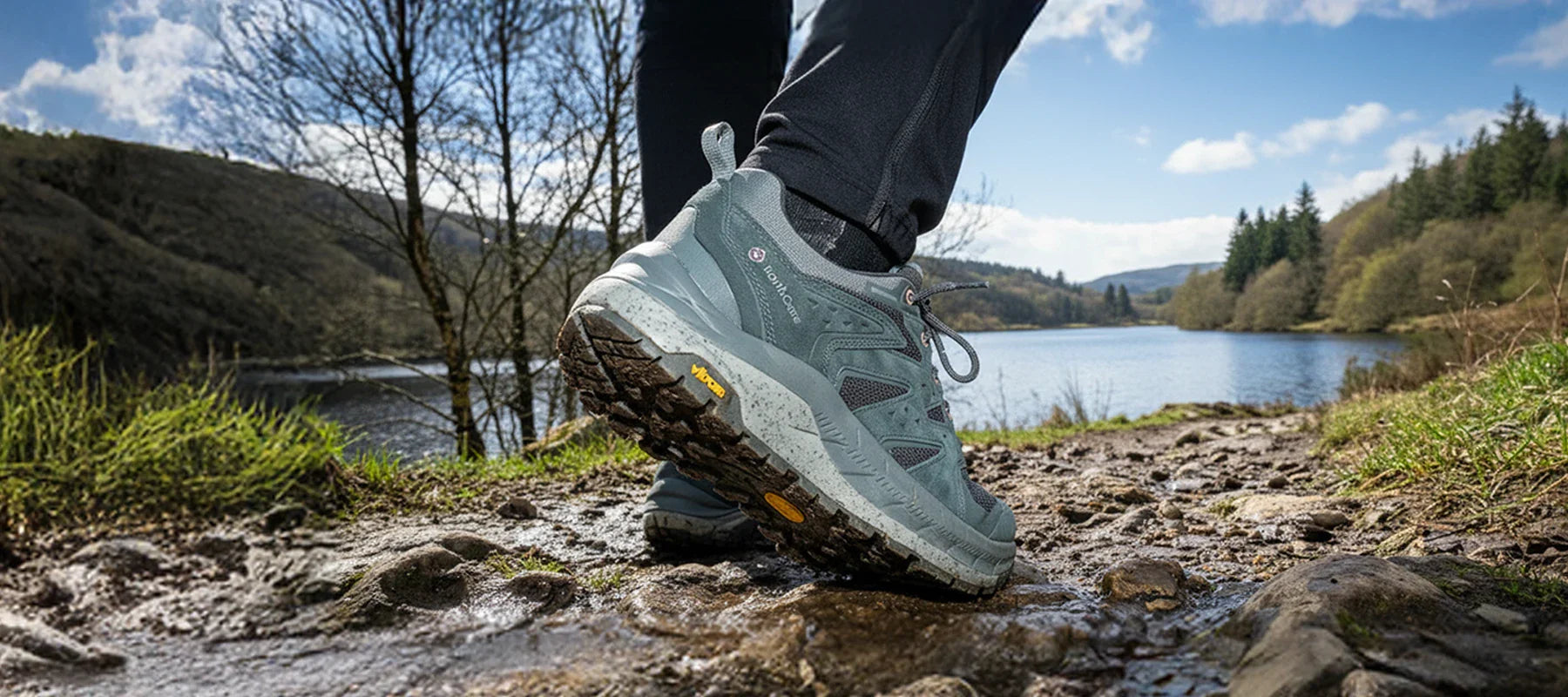 Side profile view of women's walking boot on lakeside walking trail with hills and trees in background